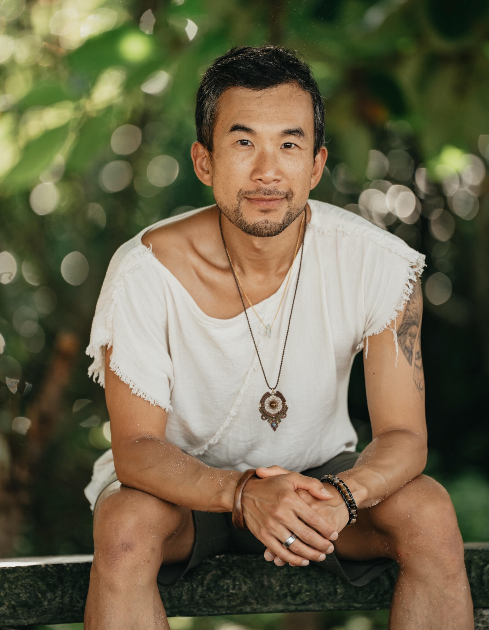 Edmond Lau seated in a forest, hands clasped, smiling softly